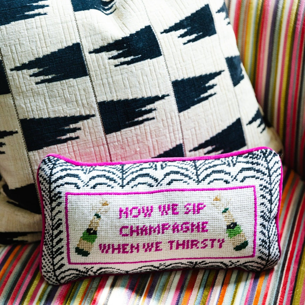  a closer look at the luxe rose velvet chic hand needlepoint pillow with "Now we sip champagne when we thirsty" saying in front sitting on a coach with a pillow 