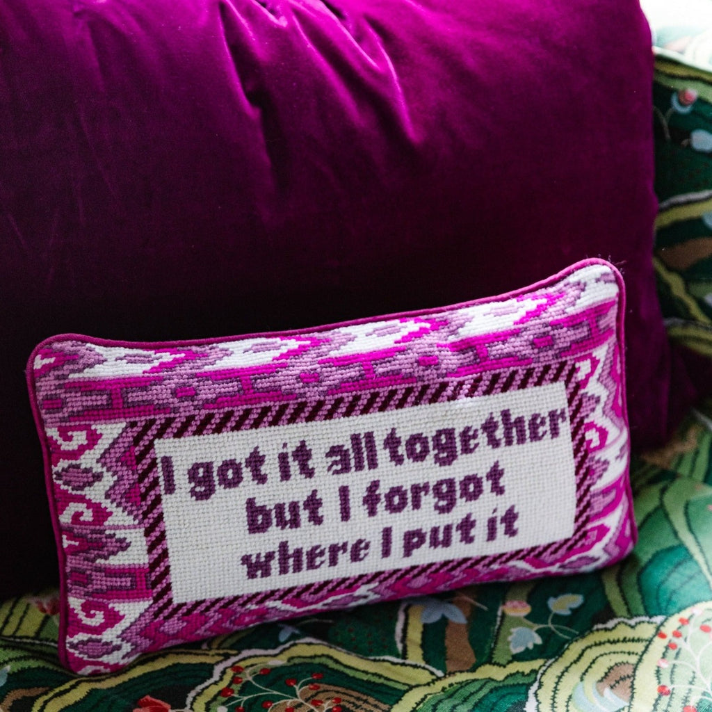 a closer look of a hand embroidered in wool and backed in luxe plum velvet chic needlepoint pillow with "I got it all together but I forgot where I put it" cheeky saying in front sitting on a couch with a plum lumbar pillow behind it