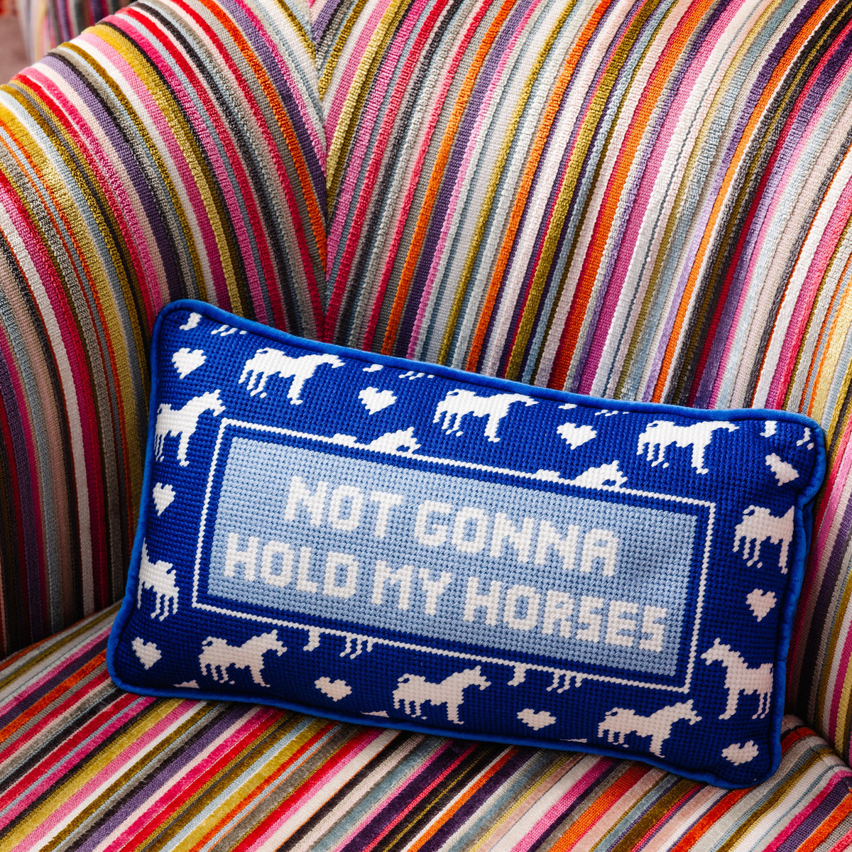 Blue pillow with horse pattern and text 'Not Gonna Hold My Horses' on a striped couch.