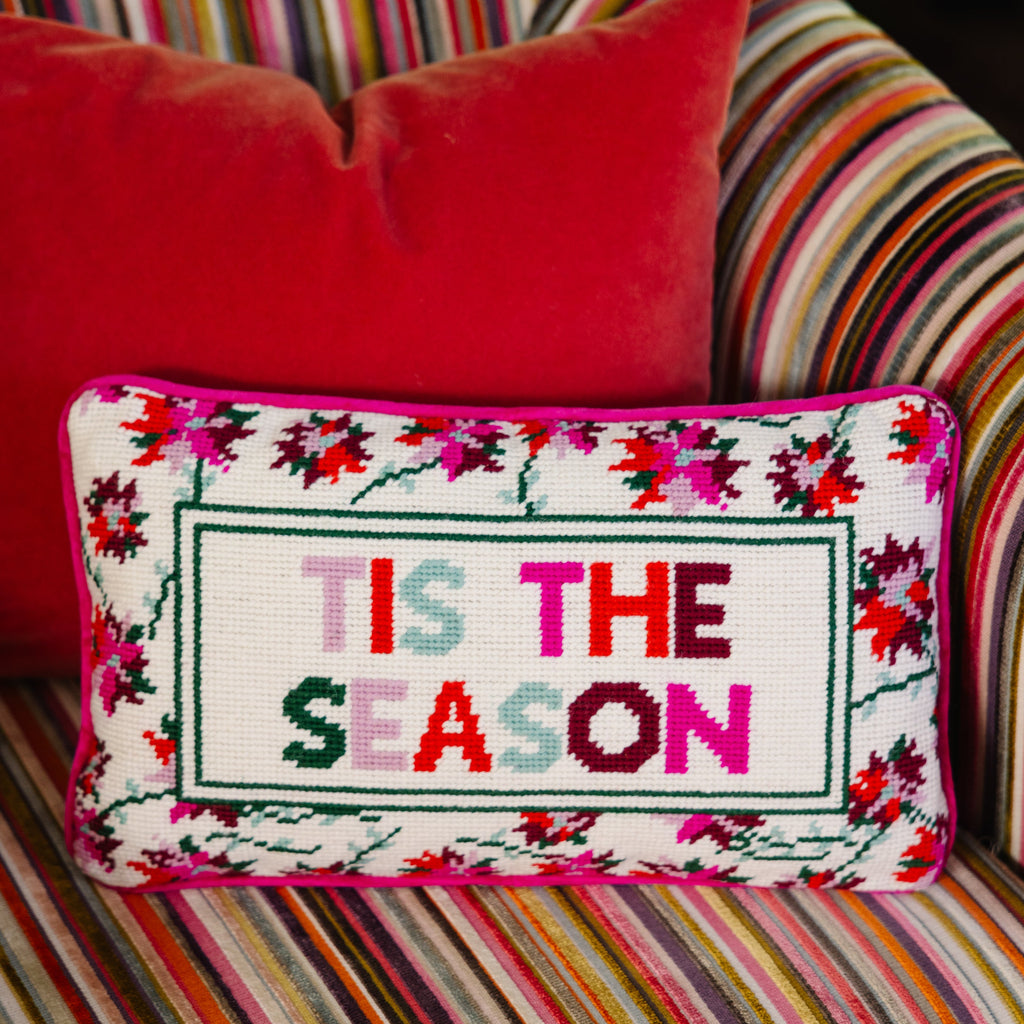 Decorative pillow with 'TIS THE SEASON' text on a colorful striped couch.