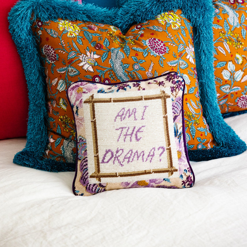 Colorful pillows on a bed with a decorative pillow reading 'Am I the Drama?'