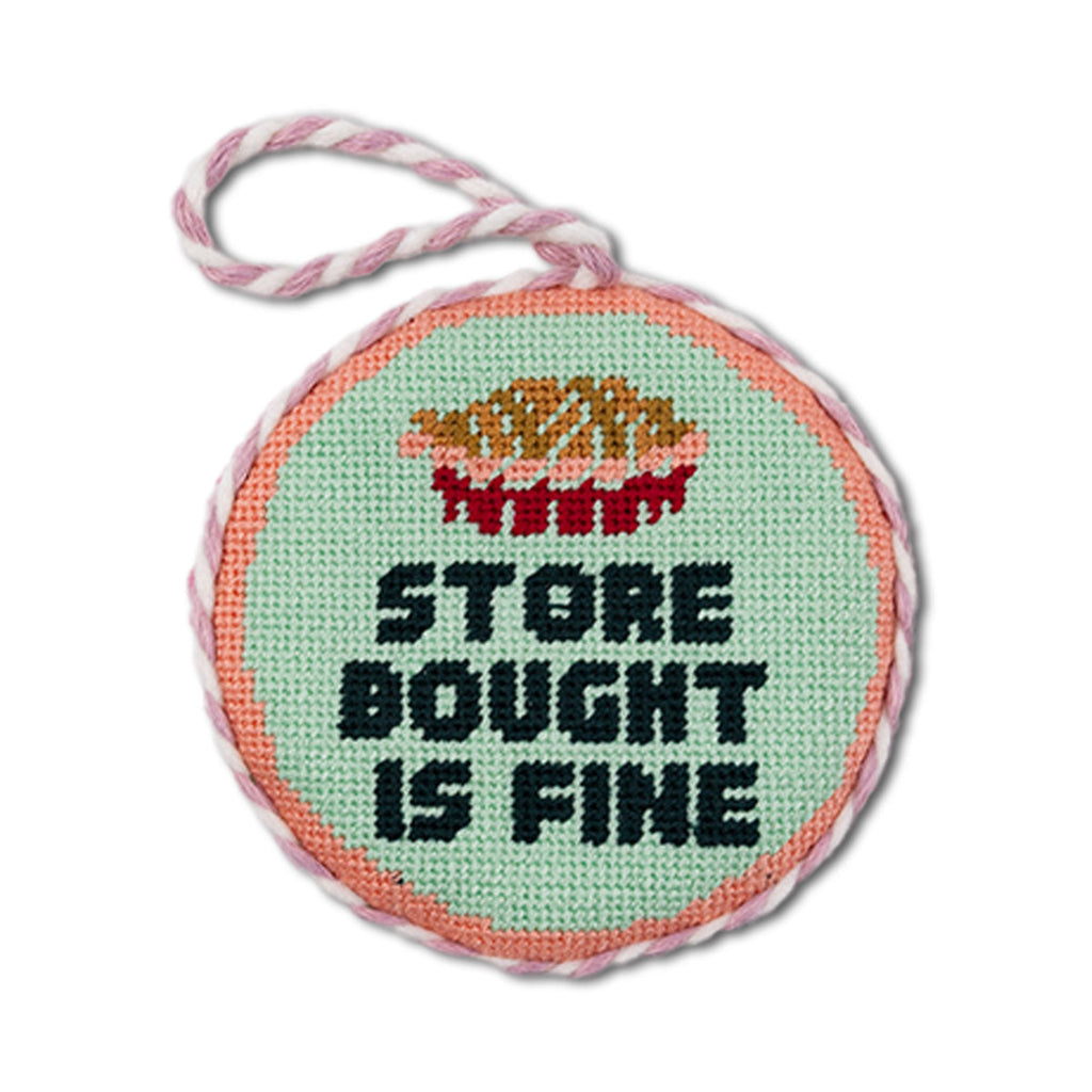 Round needlepoint ornament with text 'Store bought is fine' on a white background