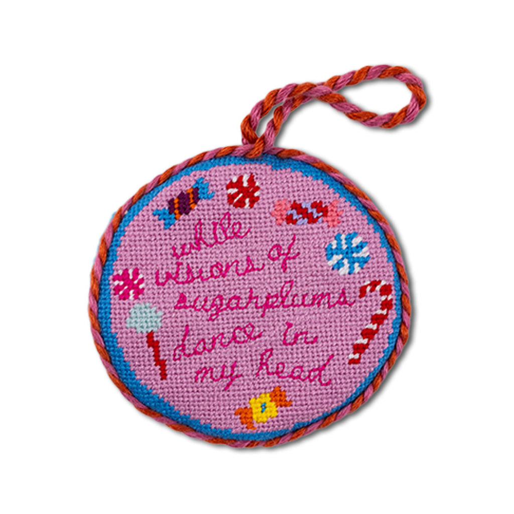 Round pink needlepoint ornament with colorful text and designs on a white background