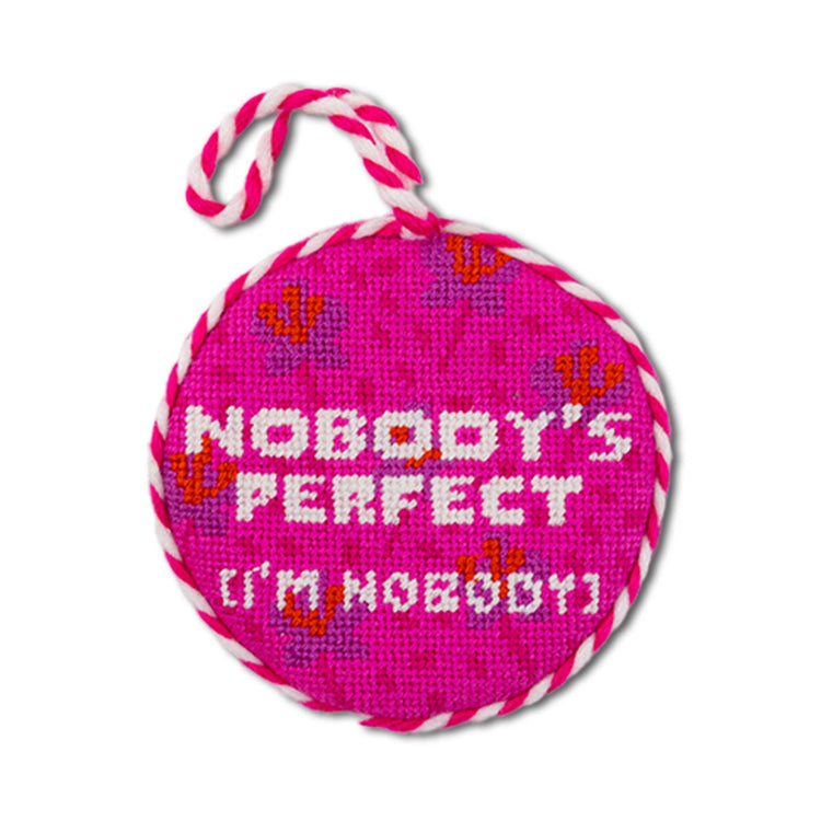 Pink round needlepoint ornament with 'Nobody's Perfect I'm Nobody' text on a white background