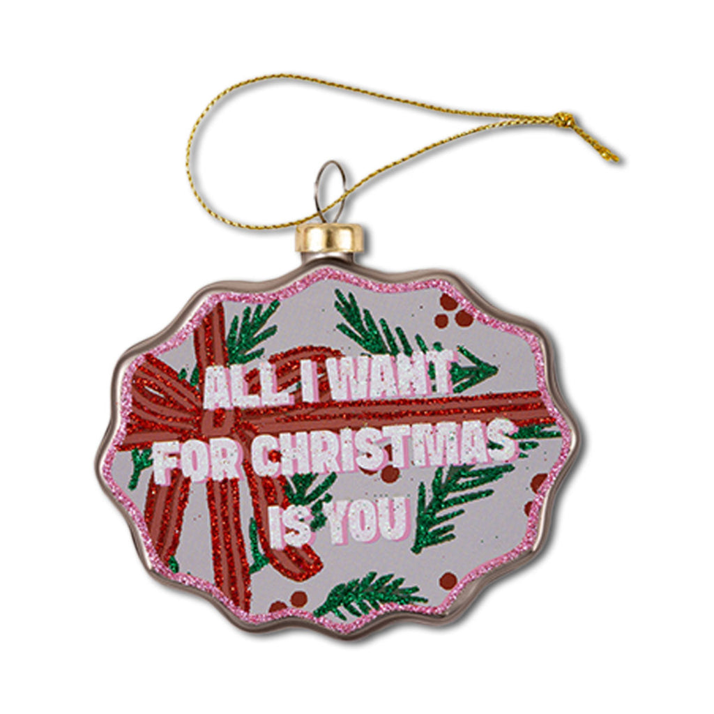 A Christmas ornament with a scallop shape, featuring text 'All I Want for Christmas Is You' with red and green decorative elements and a green holly pattern.