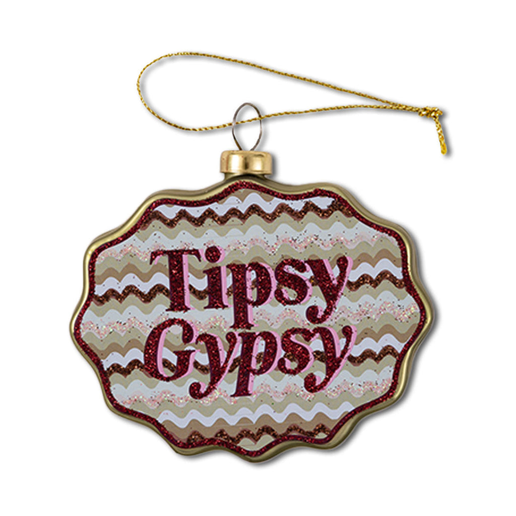 A glass ornament with a scallop shape featuring text 'Tipsy Gypsy' on a decorative background.