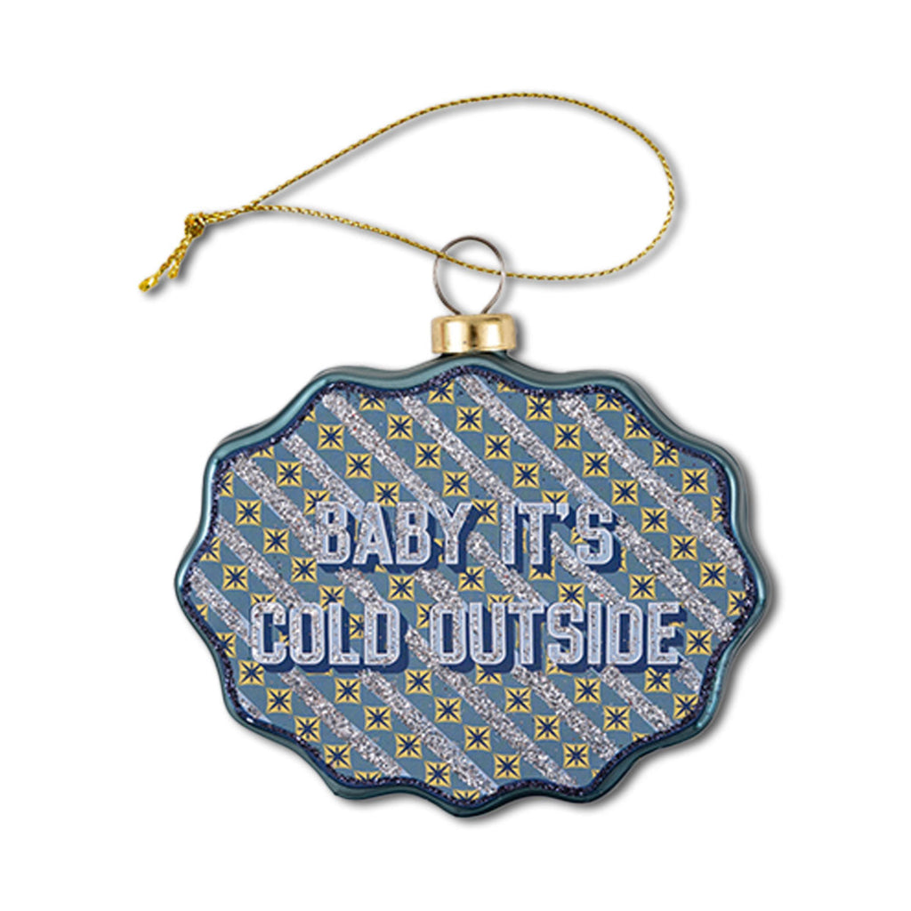 A blue glass ornament with a scalloped shape featuring the text 'BABY IT'S COLD OUTSIDE' with a patterned design behind the text.