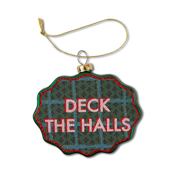 A scalloped glass ornament with a green and red pattern, featuring the text 'DECK THE HALLS' in white letters.