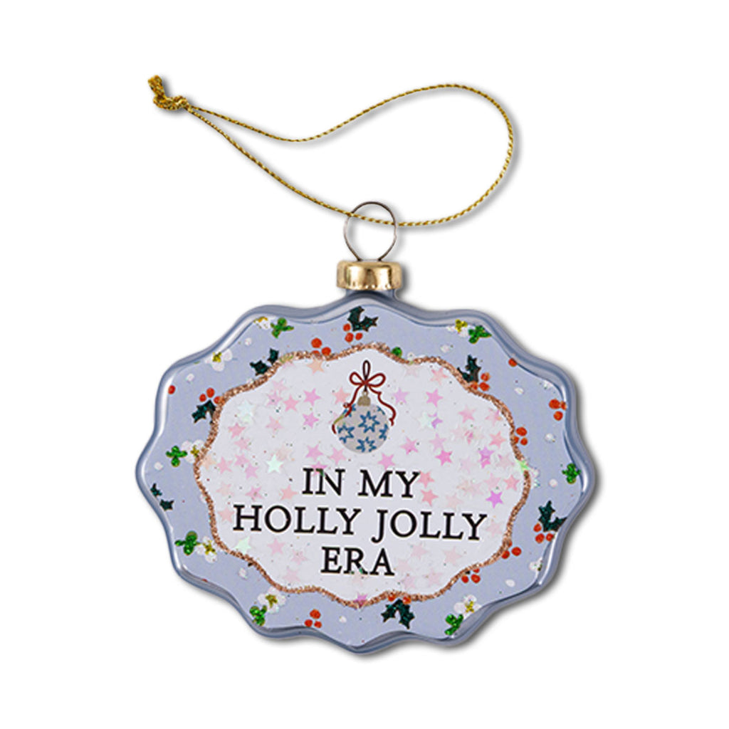 A scalloped glass ornament with a Christmas theme, featuring text 'IN MY HOLLY JOLLY ERA' on a round blue background with red and green accents and a holly design.