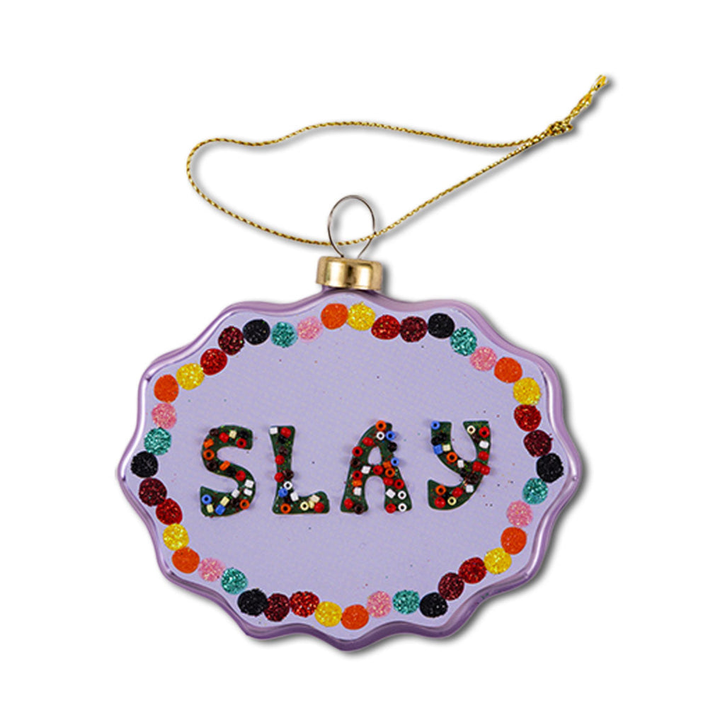 A scallop-shaped glass ornament with a purple background and the word 'SLAY' written in the center, surrounded by a multicolored border.