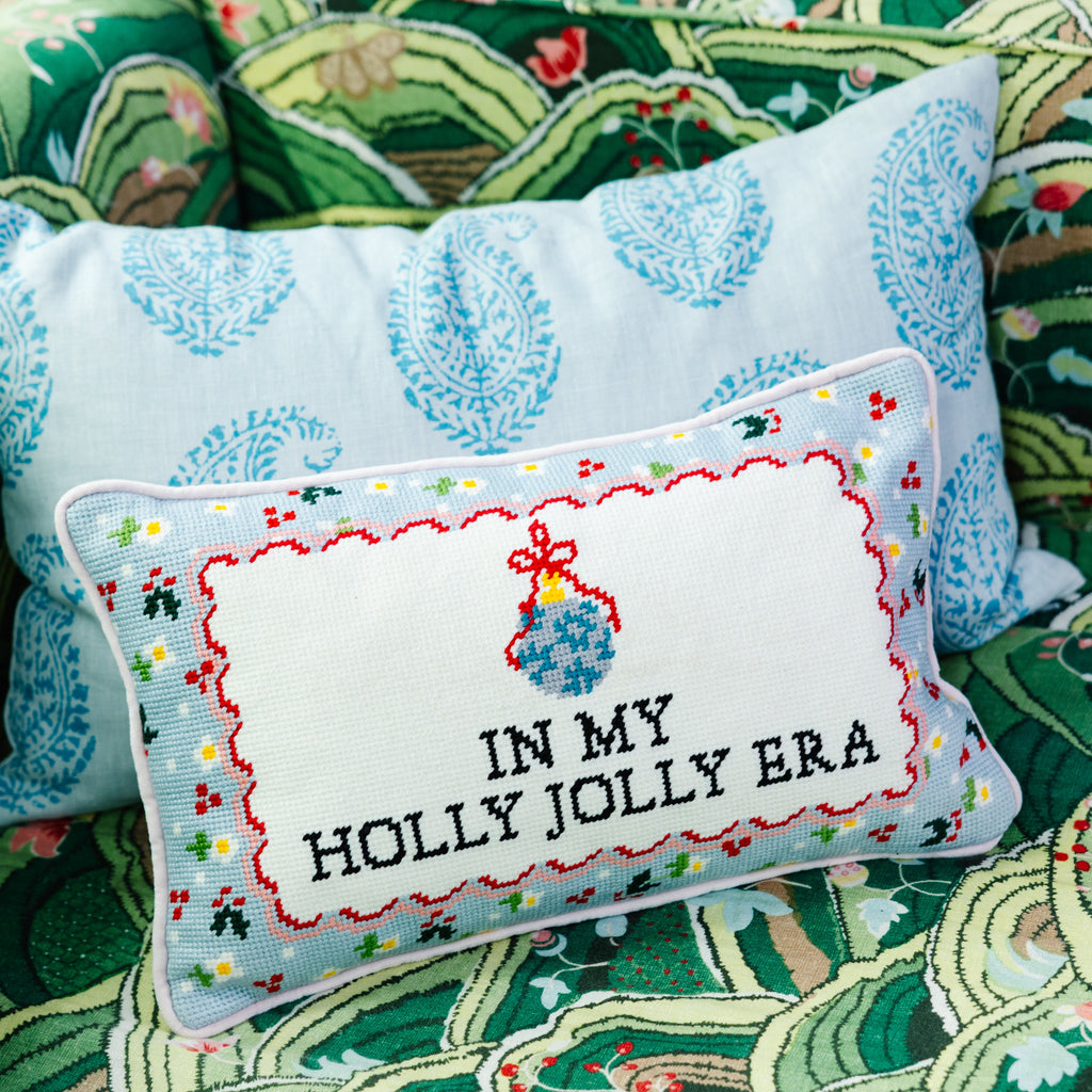 Decorative pillow with 'In My Holly Jolly Era' text on a patterned fabric background