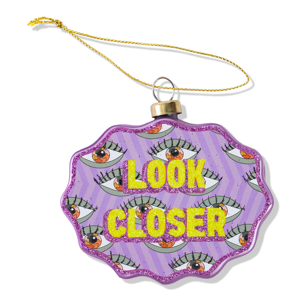 Decorative ornament with 'Look Closer' text and eye designs on a purple background.