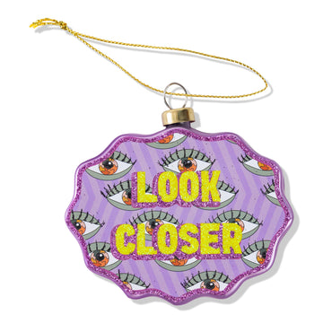 Decorative ornament with 'Look Closer' text and eye designs on a purple background.