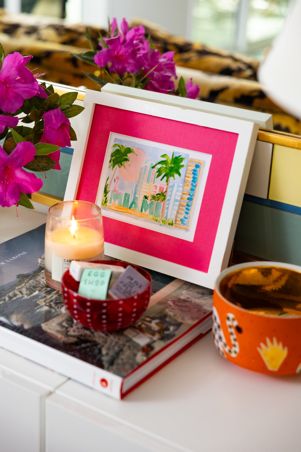 Framed artwork with pink border on a surface with books and decorative items.