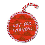 Round red object with brown pattern and 'Not for Everyone' text, tied with red and white string on a white background.