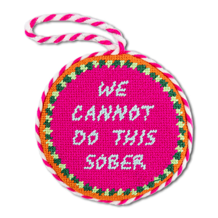 Circular pink sign with 'WE CANNOT DO THIS SOBER' text, surrounded by colorful border and string handle.