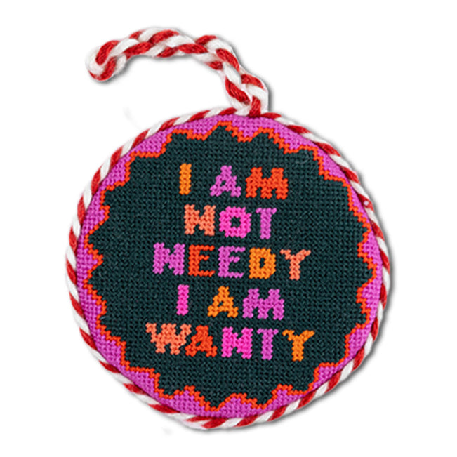 Round needlepoint ornament with colorful text and braided handle on a white background