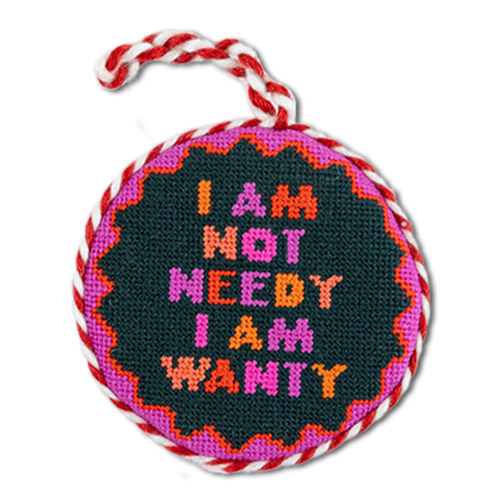 Round needlepoint ornament with colorful text and braided handle on a white background