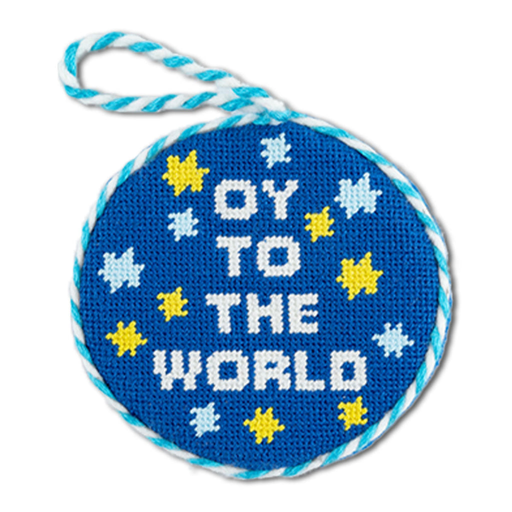 Circular blue needlepoint with 'OY TO THE WORLD' text and star patterns on a white background