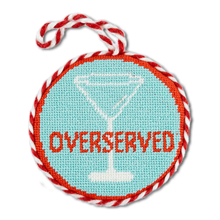 Round needlepoint ornament with 'Overserved' text and martini glass design, wrapped in red and white string.