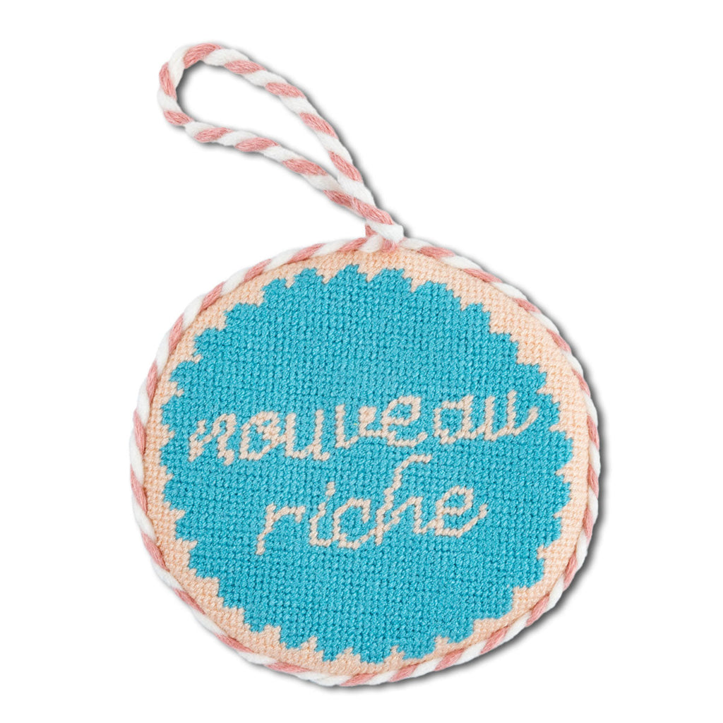 Round needlepoint ornament with 'nouveau riche' text on a white background