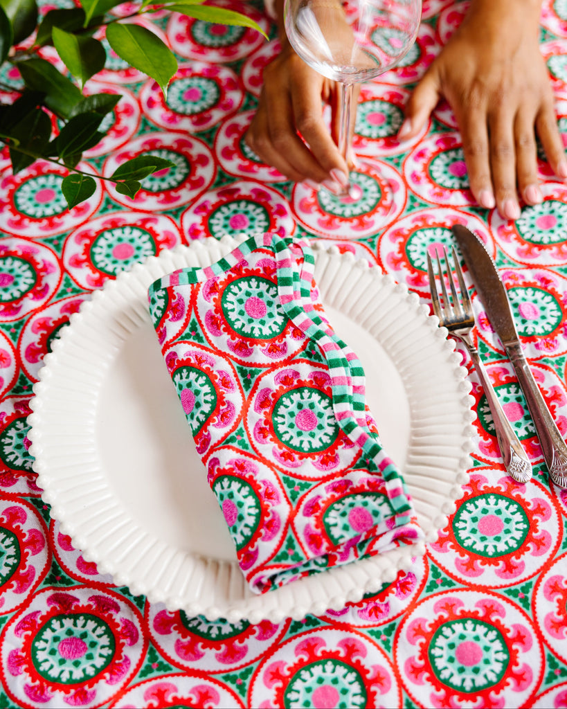 Person setting a table with a colorful napkin and cutlery on a patterned tablecloth.