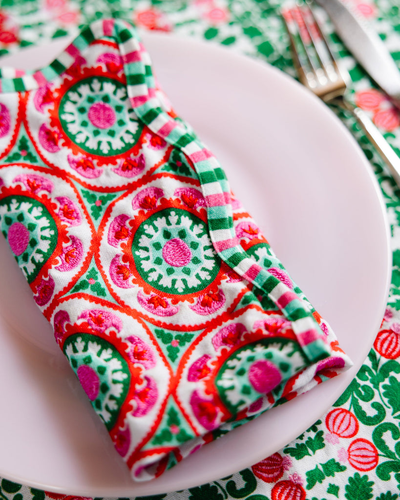Colorful patterned napkin on a white plate with cutlery on a matching tablecloth.