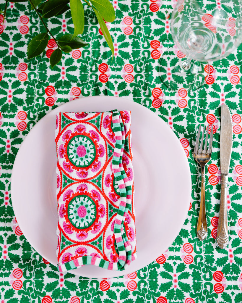 Table setting with a patterned napkin, plate, and cutlery on a green and pink floral tablecloth.
