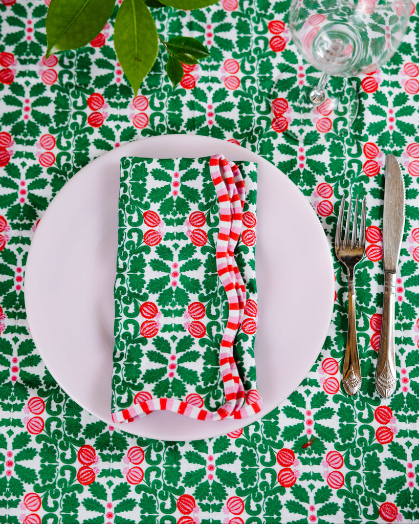 Christmas-themed table setting with a red and green patterned tablecloth, white plate, striped red and white napkin, and cutlery.