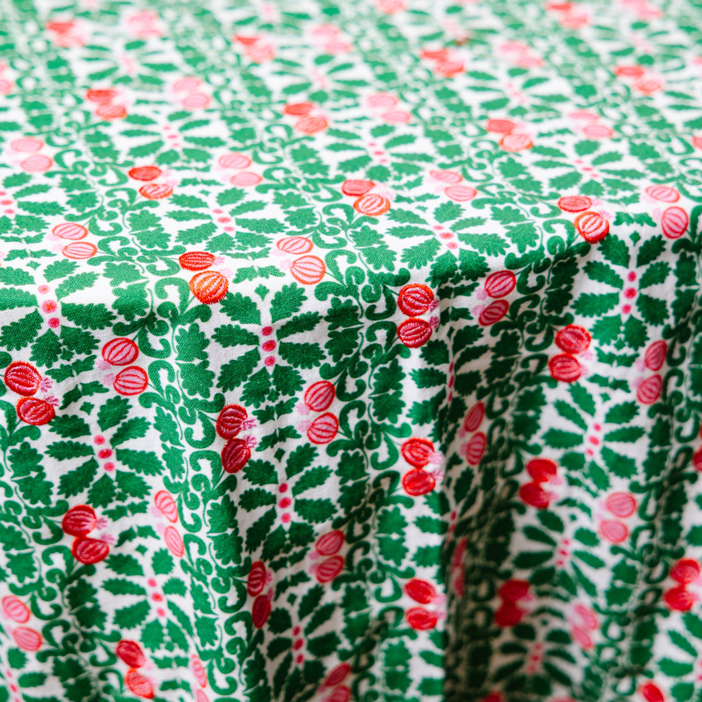 Close-up view of a round tablecloth with a green base and red pomegranate patterns.