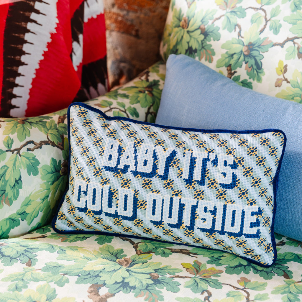 Decorative pillows with text and patterns on a floral-patterned couch against a brick wall.
