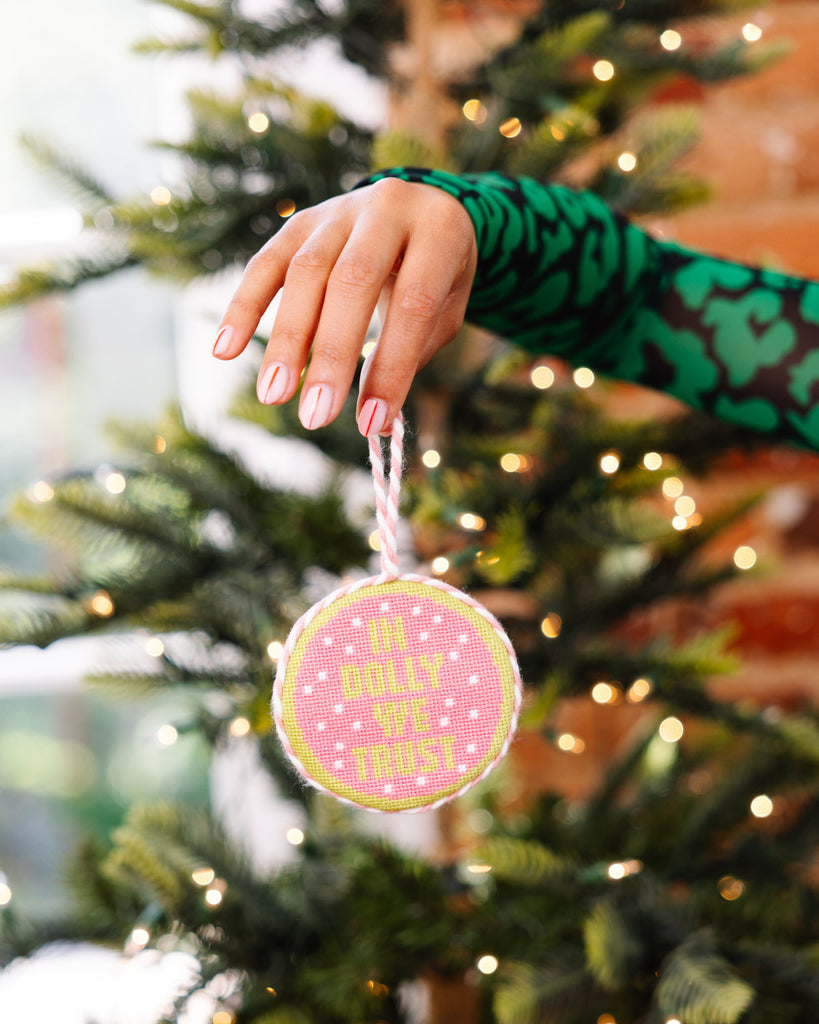 Hand hanging a pink ornament with text on a decorated Christmas tree.