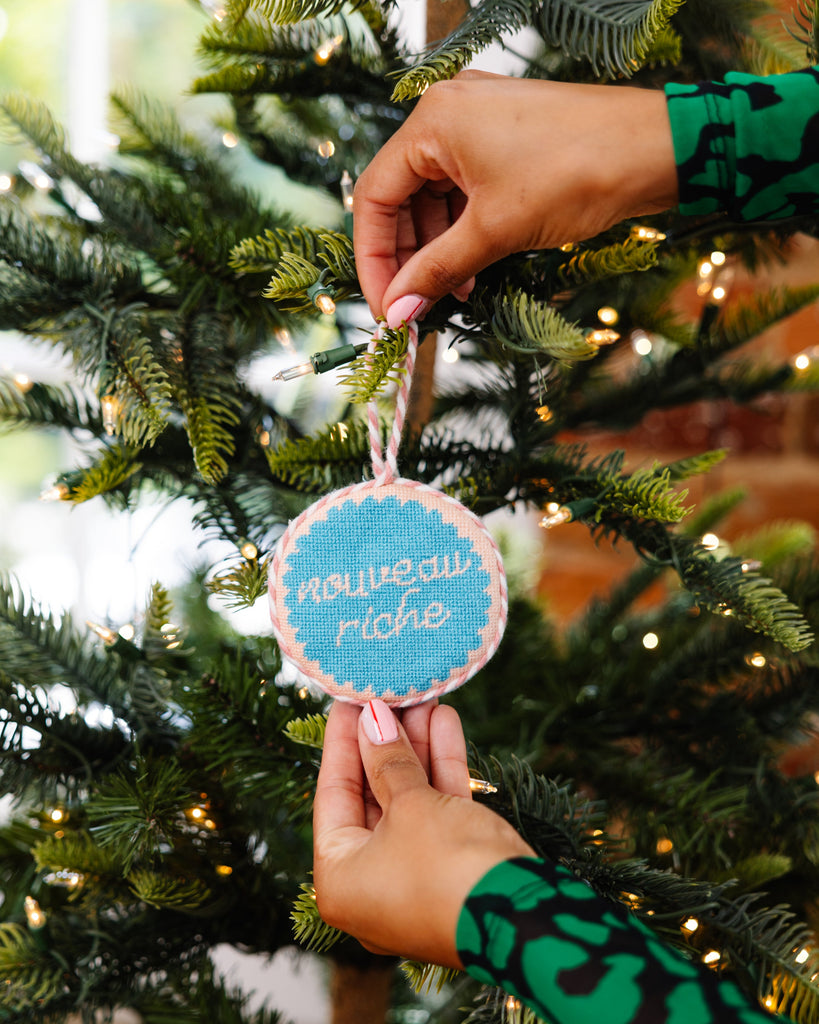 Person hanging a Christmas ornament on a tree with blurred lights in the background