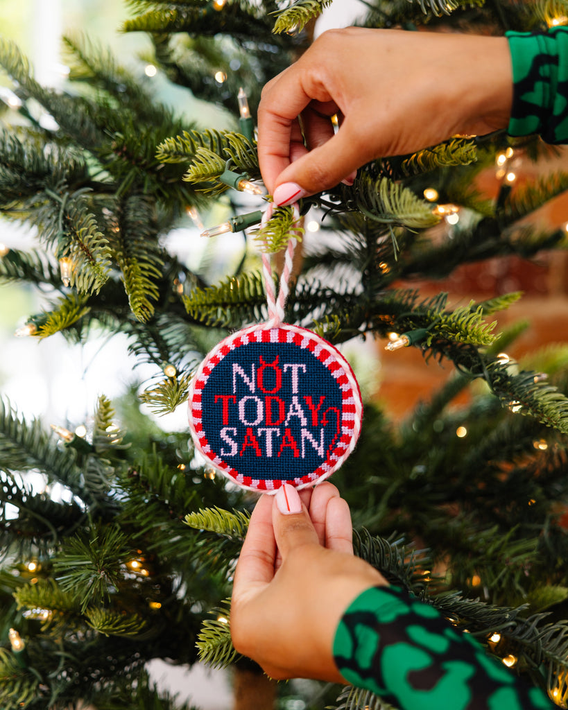 Hand hanging a 'Not Today, Satan' ornament on a Christmas tree.