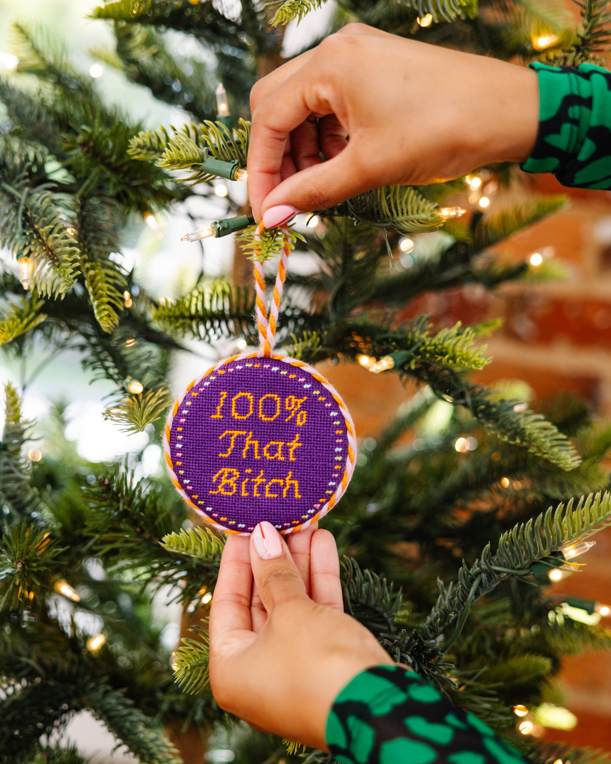 Person hanging a decorative ornament with text on a Christmas tree.