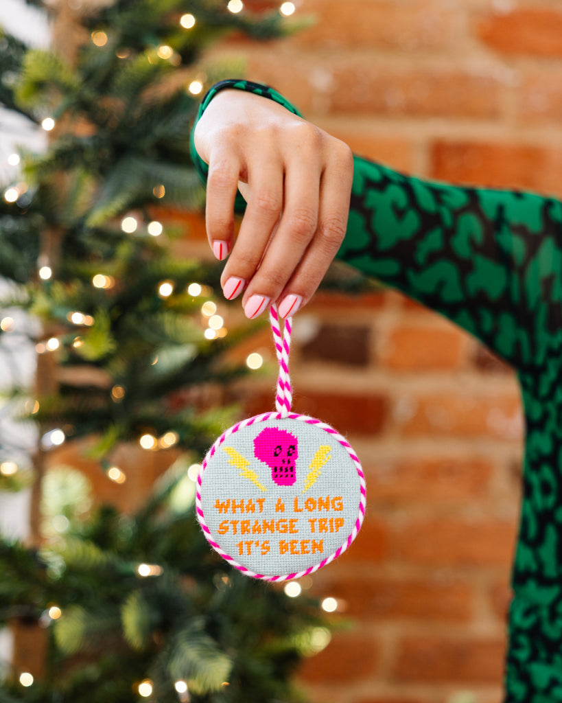 Person holding a Christmas ornament with text in front of a decorated tree.