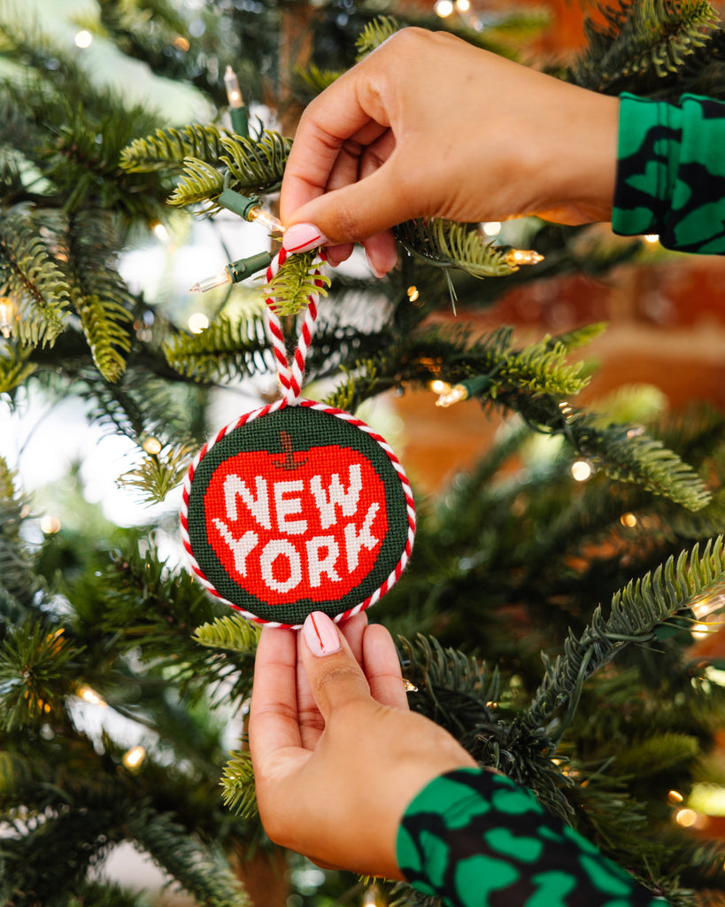 Person holding a 'New York' ornament on a Christmas tree