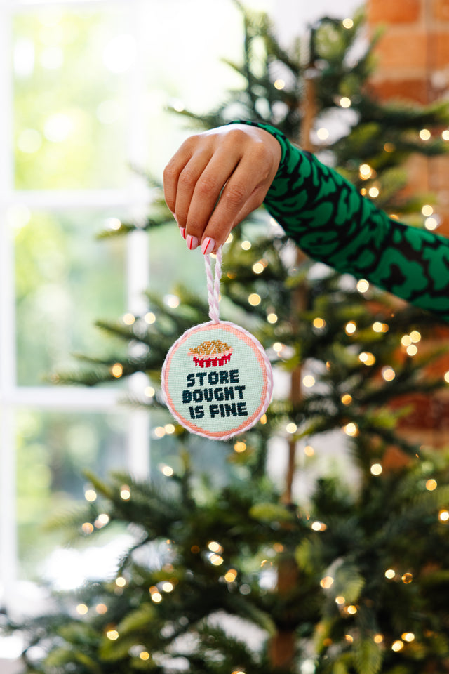 Hand holding a Christmas ornament with text in front of a decorated tree