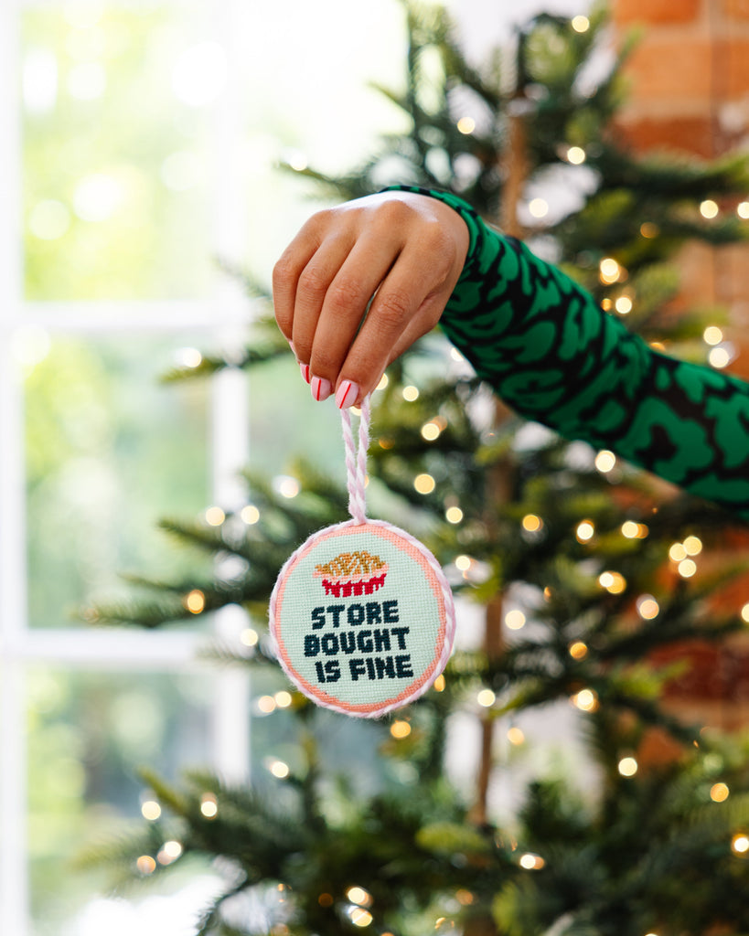 Hand holding a Christmas ornament with text in front of a decorated tree