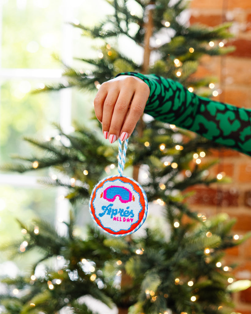 Hand holding a Christmas ornament with a colorful design in front of a decorated tree.