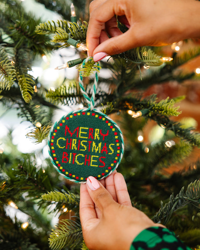 Person holding a 'Merry Christmas Bitches' ornament on a decorated tree