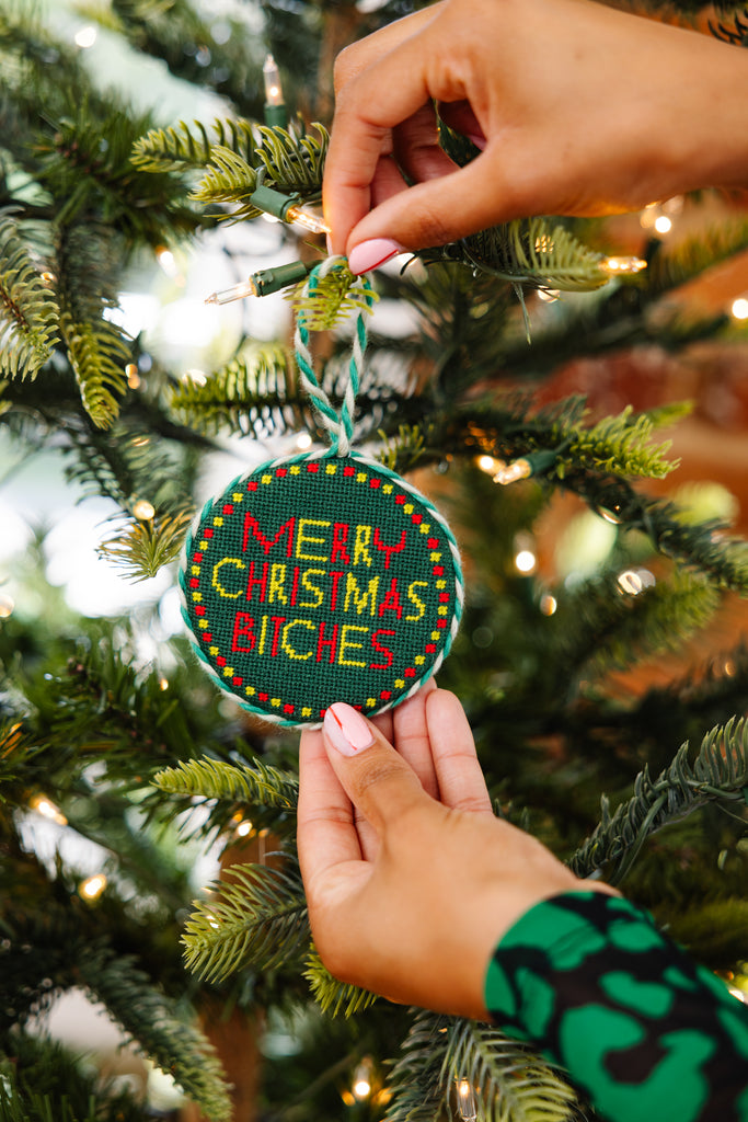 Person holding a 'Merry Christmas Bitches' ornament on a decorated tree