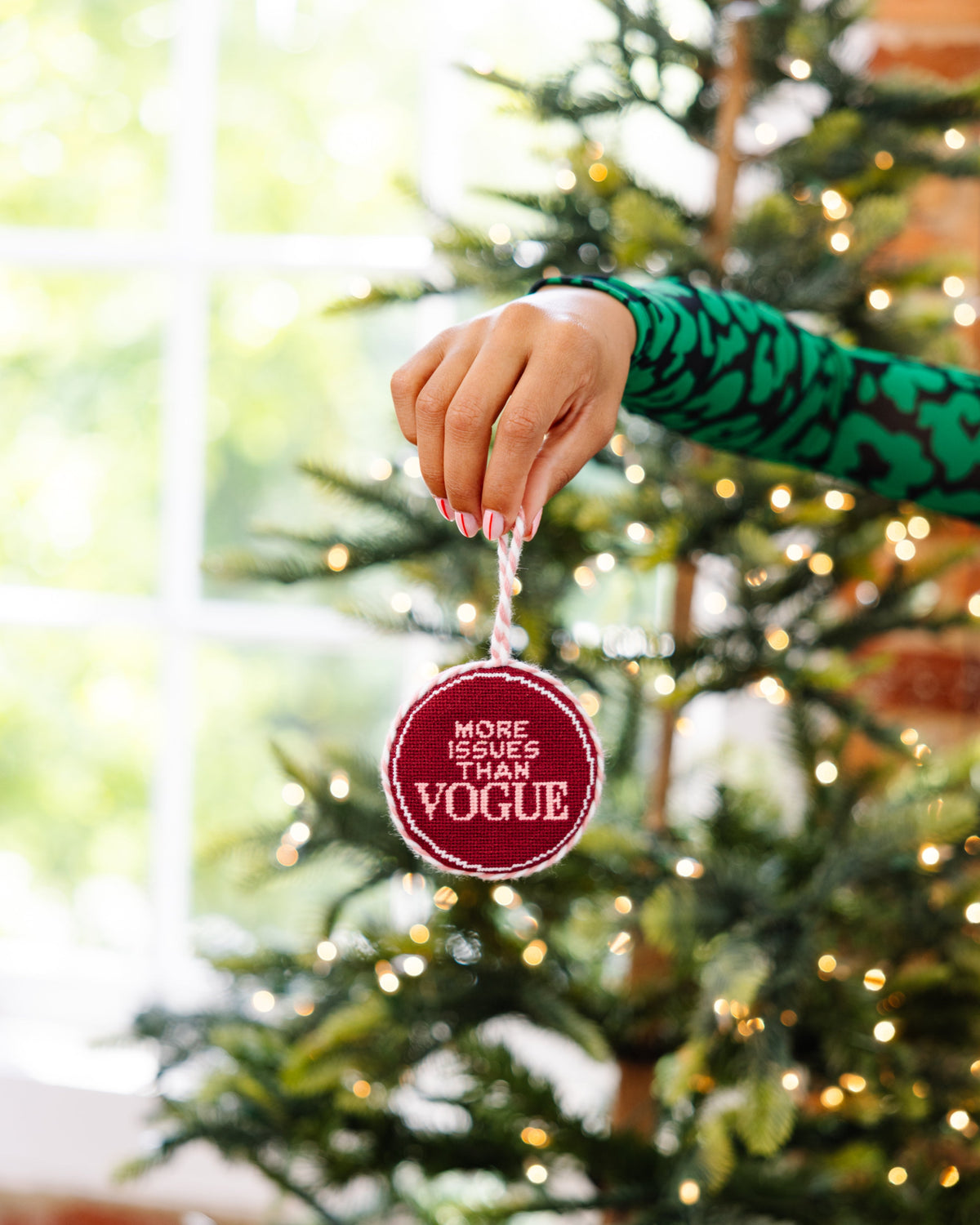 Hand placing a 'More Issues Than Vogue' ornament on a Christmas tree.