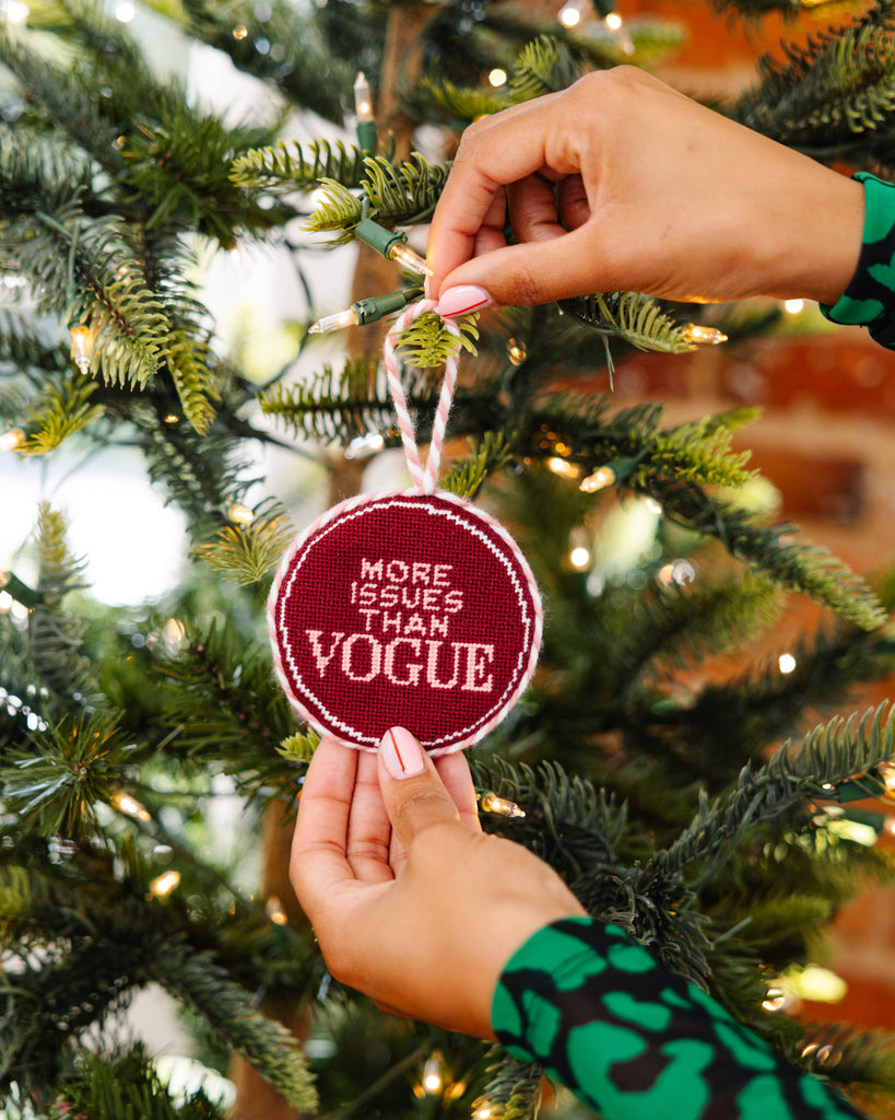 Person hanging a decorative ornament on a Christmas tree with text 'More issues than Vogue'.