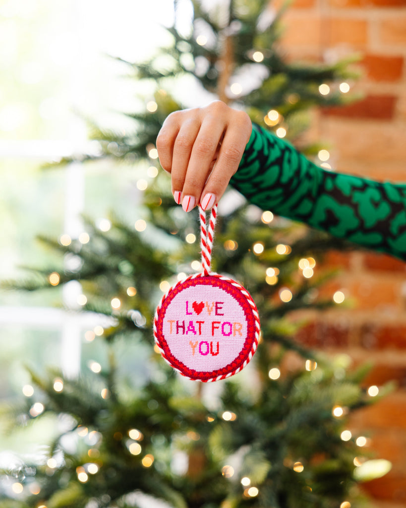 Hand holding a Christmas ornament with 'Love that fo you' text in front of a decorated tree.