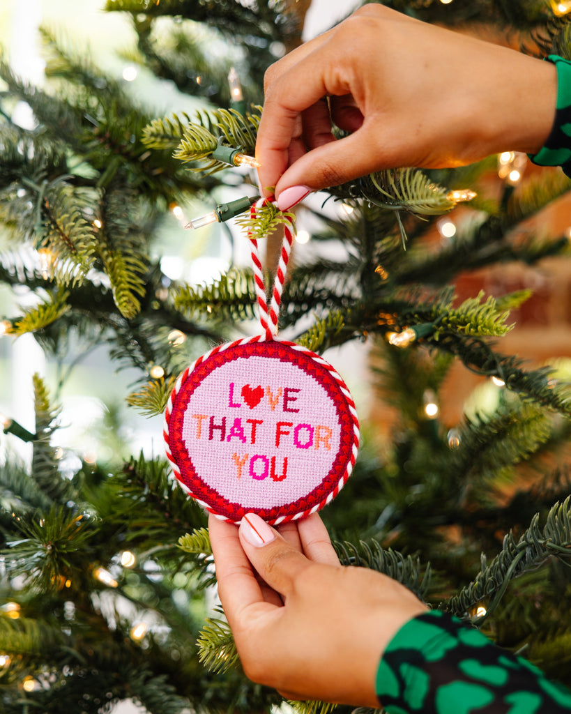 Hand holding a Christmas ornament with 'Love That For You' text on a decorated tree.
