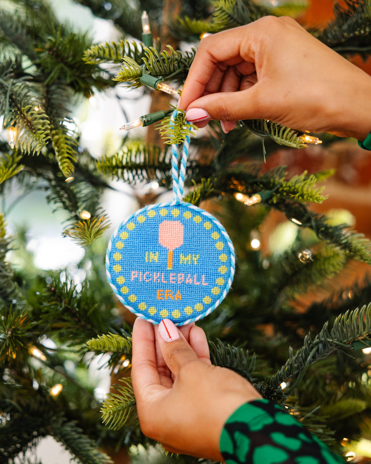 Hand placing a Christmas ornament with text on a tree