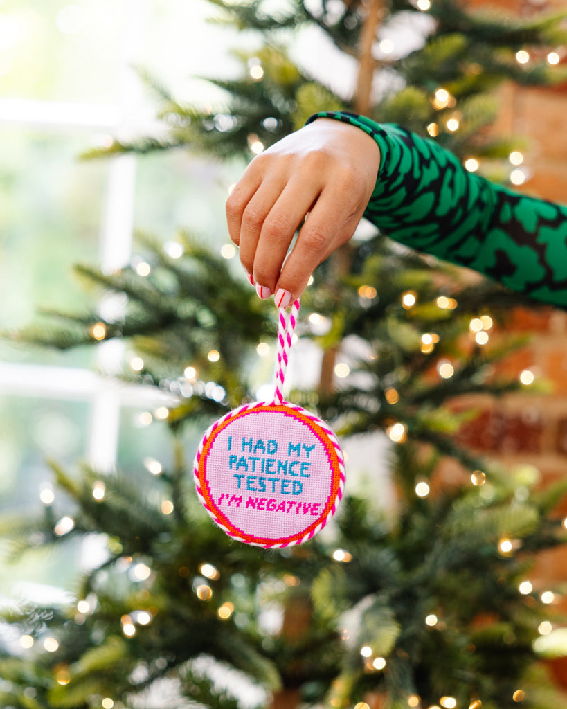 Hand holding a Christmas ornament with text in front of a decorated tree