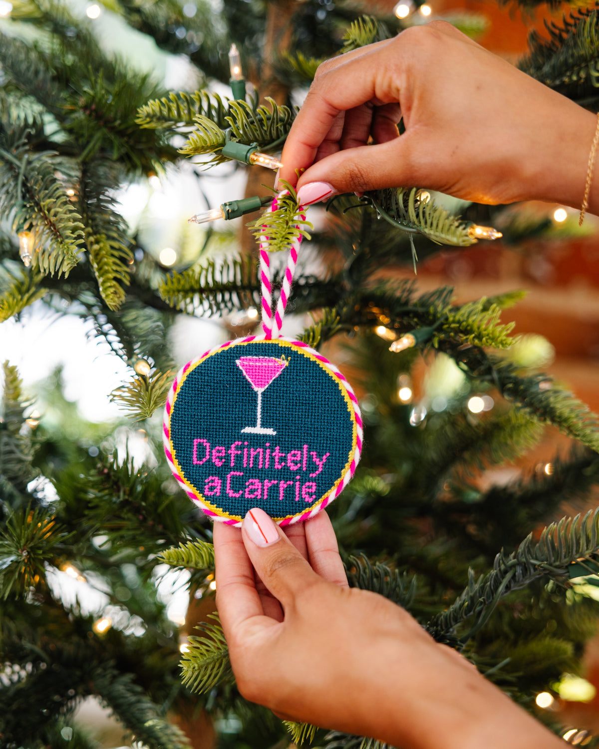 Hand holding a Christmas ornament with 'Definitely a Carrie' text against a decorated tree background