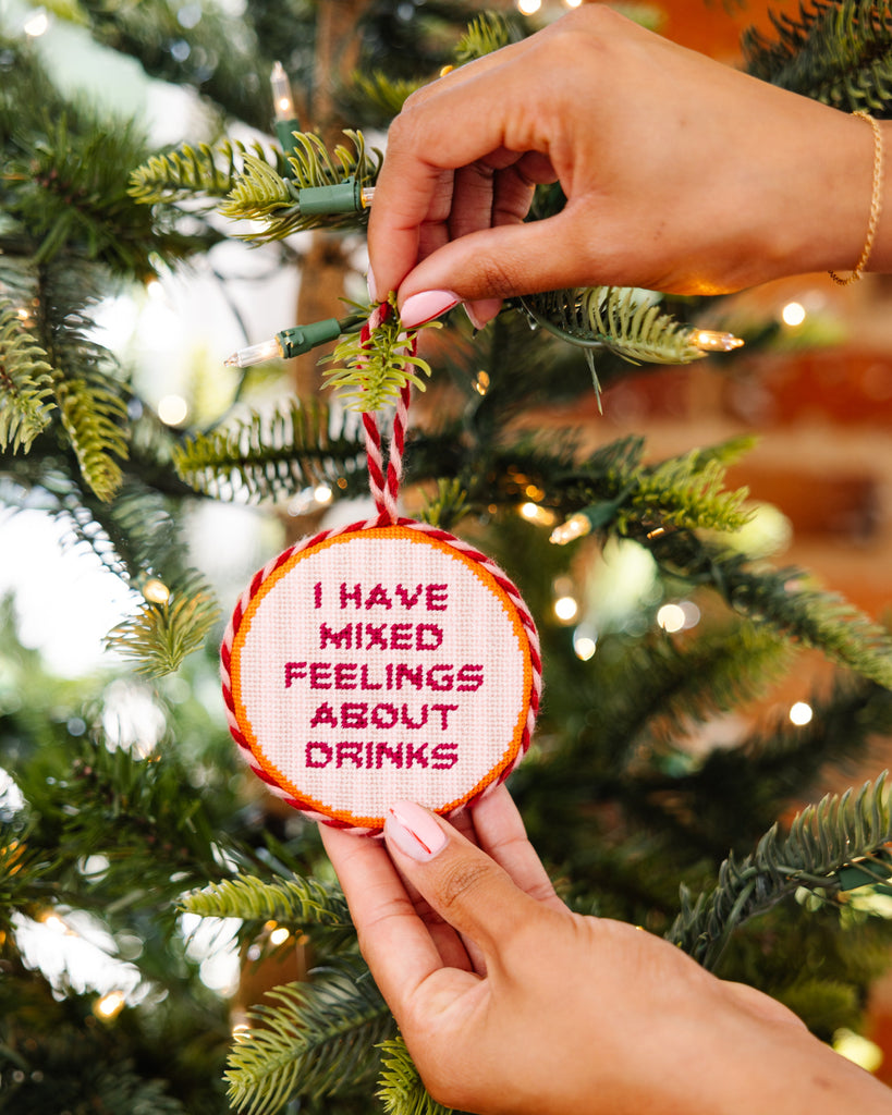 Hand holding a Christmas ornament with text 'I have mixed feelings about drinks' against a festive background.